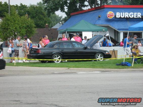 Black sedan parked with hood open, people gathered around. Burger King in background