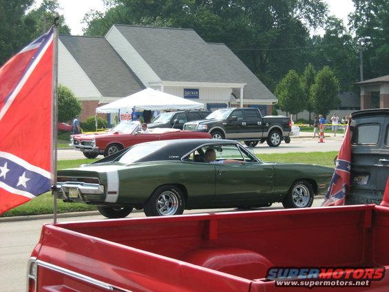 Green 1970 Dodge Charger with a white stripe on the side, parked next to a red convertible and a black pickup truck