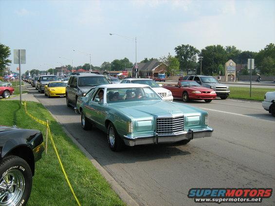 Light blue 1977 coupe with white roof, front grille, and chrome bumper in traffic