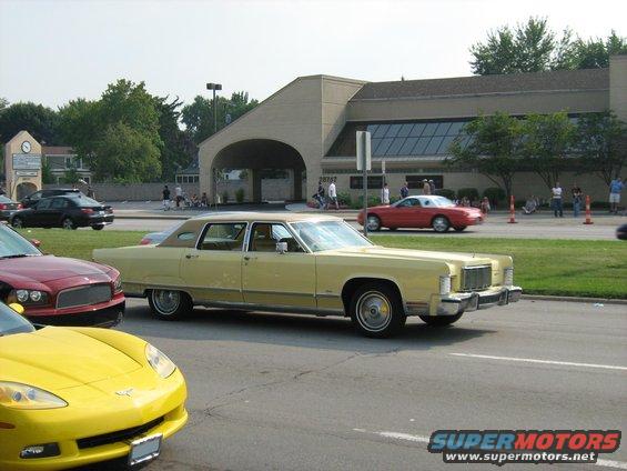 Yellow 1977 Mercury Grand Marquis sedan parked on street, red car and yellow sports car nearby