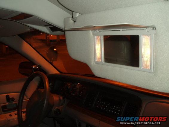 Interior shot of a car, showing the steering wheel, dashboard, and a lighted vanity mirror on the sun visor