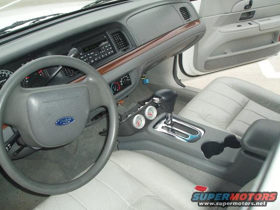 Interior of a 2003 Ford Crown Victoria showing the dashboard, steering wheel, center console with gear shifter and gauges, and leather seats