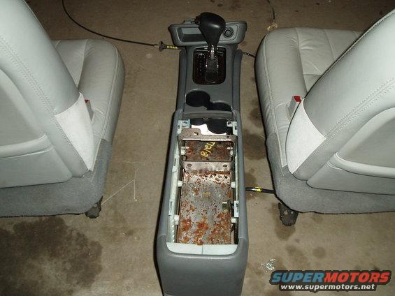 Car interior with gray seats and center console removed, showing rusty metal components