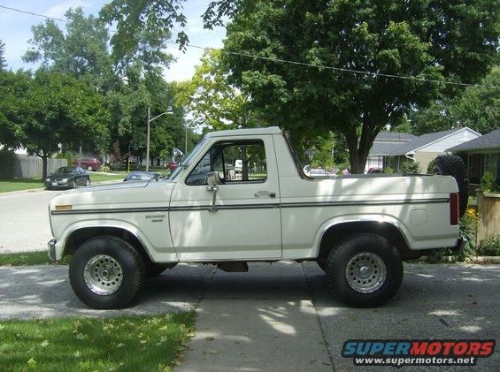 White Ford Bronco parked on a residential street. Side view shows the full body, wheels, and spare tire on the back
