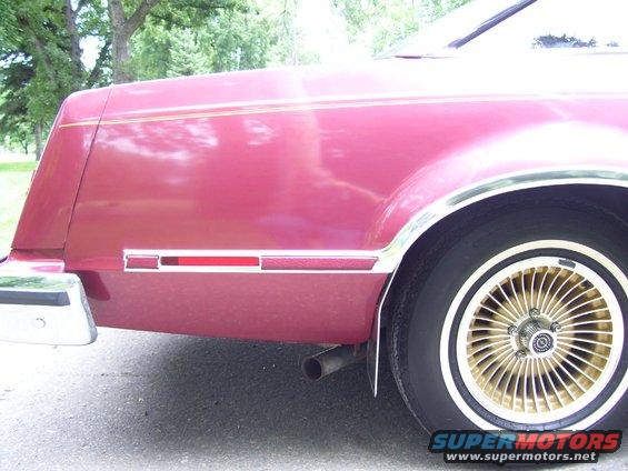 Rear side of a maroon car with gold turbine wheels and a chrome bumper
