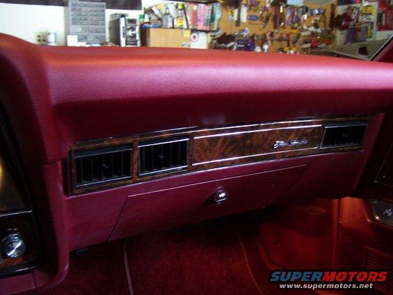Red car interior dashboard with wood grain trim and air vents. "Elite" text visible
