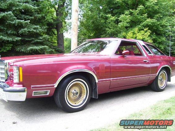 Maroon coupe with gold wheels, side view. Appears to be a 1977 Ford Thunderbird