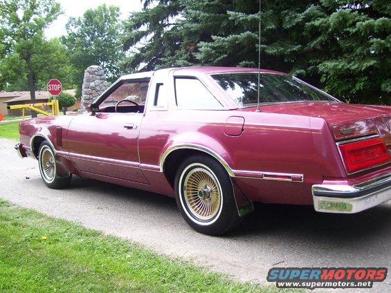 maroon coupe parked on a gravel driveway, trees and a stop sign in background
