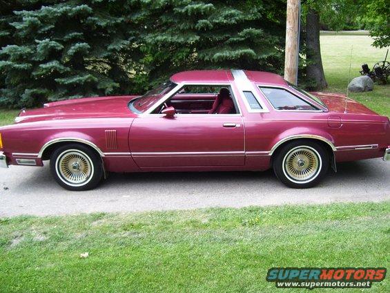 Maroon coupe with a silver T-top roof, gold wire wheels, and chrome trim, parked on a paved surface next to grass
