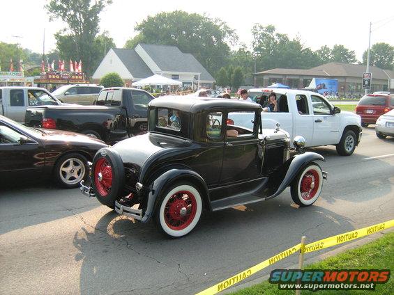 Antique black coupe with red wheels and whitewall tires, spare tire on rear, seen from the rear 3/4 angle