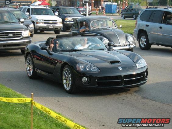 Black convertible sports car with a hood scoop and chrome wheels, seen from the front