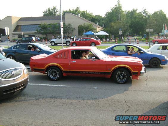 Red coupe with 'Road Runner' decal driving in traffic. Other cars visible