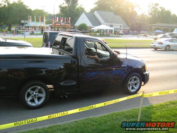 Black pickup truck with blue lightning graphics, side view. Another vehicle is partially visible behind it