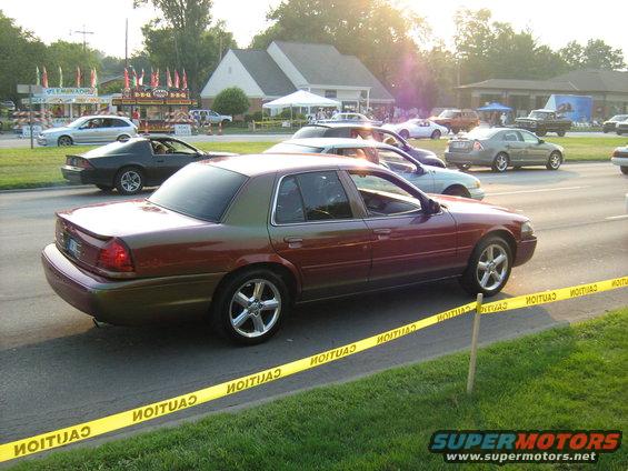Side view of a maroon and tan sedan, possibly a Crown Victoria, driving past caution tape