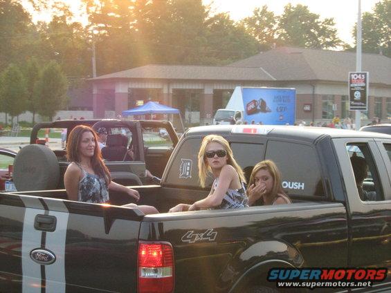 Three women in the bed of a Ford pickup truck. Another vehicle is next to it