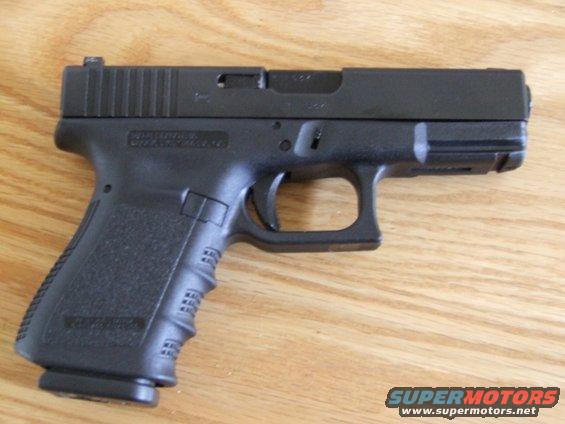 Black semi-automatic pistol with textured grip, resting on a wooden surface. Text on slide is partially visible