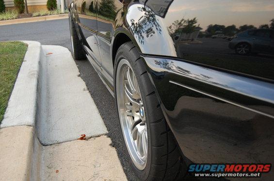 Side view of a black 2002 BMW M3 parked next to a curb. Shows the front wheel and part of the rear wheel