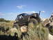 1984 Ford Bronco II - Customized truck navigates rocky terrain under a blue sky with scattered clouds.