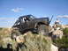 1984 Ford Bronco II - A heavily modified truck navigates a rocky trail under a blue sky with scattered clouds.