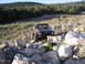 1984 Ford Bronco II - A modified black SUV with a roll cage drives over large rocks in a dry, grassy landscape.