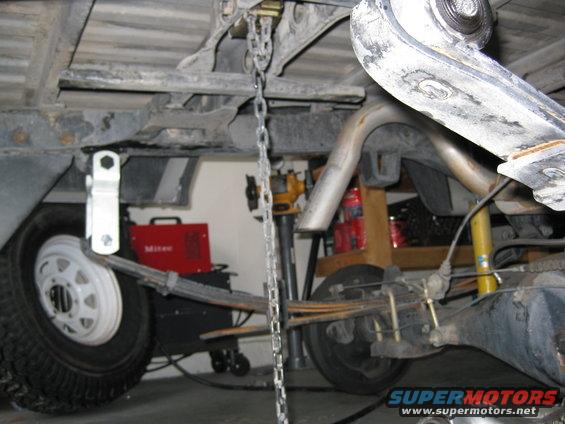 Underside of a pickup truck showing leaf springs, exhaust, and a welding machine in the background