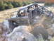 1984 Ford Bronco II - Off-road SUV with extensive roll cage modification navigates a rocky terrain.