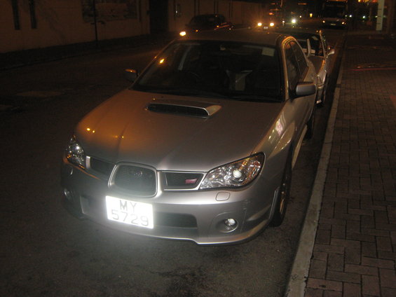 Silver Subaru Impreza WRX STI parked on a street at night, front view. License plate MY 5729
