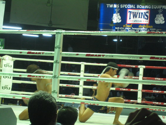 Two Muay Thai boxers training in a ring with 'Twins Special Boxing Equipment' banner overhead