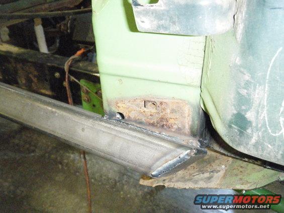 Close-up of rusted metal and fresh welds on a light green vehicle's lower body panel