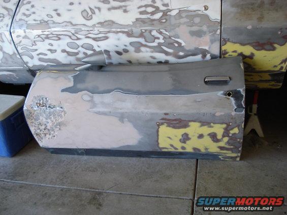 Car door and fender with body filler and primer, showing rust damage on the door's lower front corner