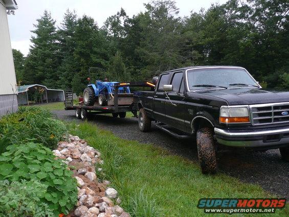 Black 1997 Ford F-350 truck, 3/4 front view, towing a trailer with a blue tractor
