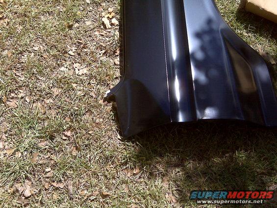 Black car fender with dented corner, resting on grass