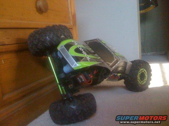 RC rock crawler with green accents on carpet next to wooden furniture