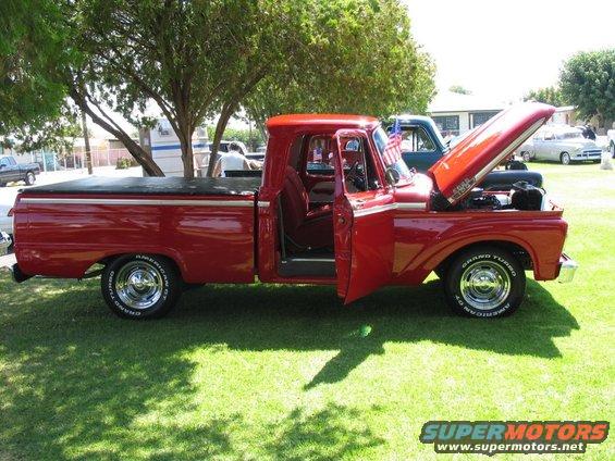 Red pickup truck with hood open and driver's door ajar, parked on grass