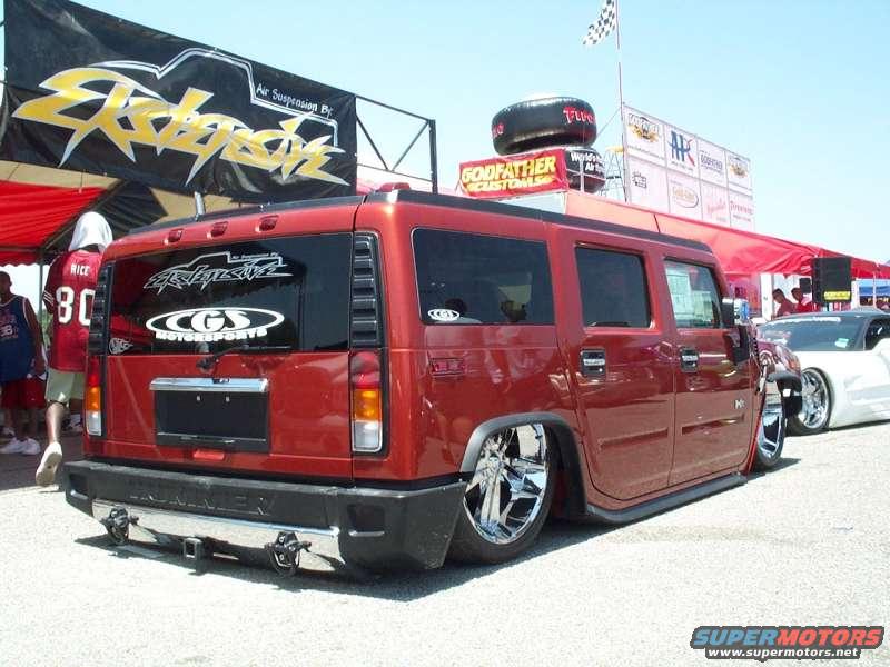 Red Hummer H2 with custom wheels, lowered suspension, and racing banners in the background