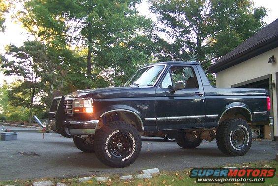 Dark blue Ford Bronco with aftermarket wheels and brush guard parked outside a garage