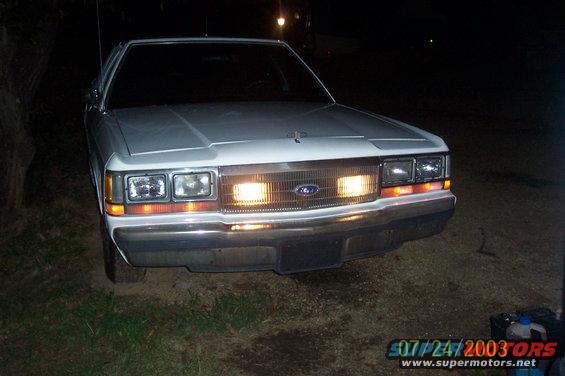Front view of a white 1991 Ford Crown Victoria LTD with headlights on