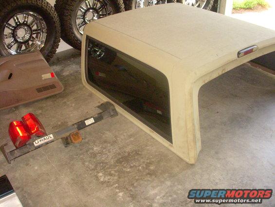 Tan Ford Bronco hardtop with tinted windows, next to a U-Haul trailer hitch and taillights