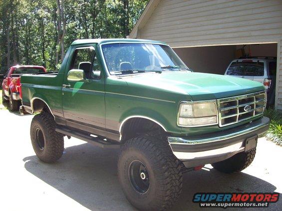 Green 1992 Ford Bronco lifted with large tires, parked in driveway. Another vehicle is visible in the garage