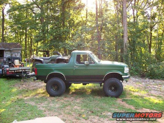 Green 1992 Ford Bronco with lifted suspension parked in a grassy area with trees