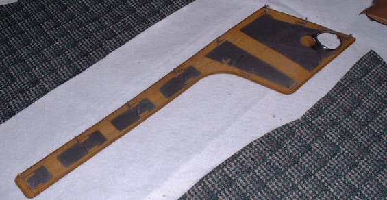 Tan interior trim piece with dark rectangular pads and a circular cutout