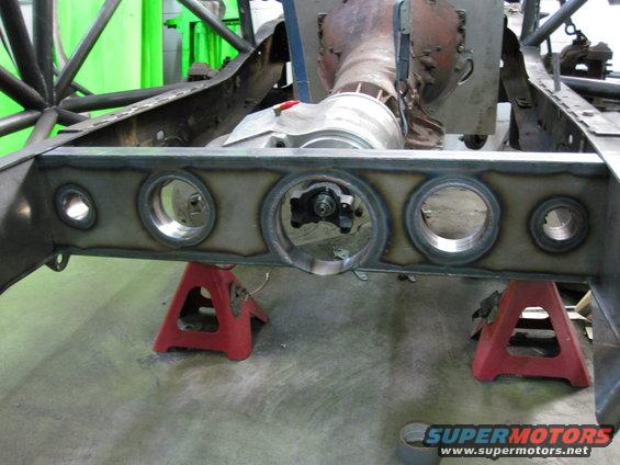 Custom rear axle housing with large circular cutouts, supported by red jack stands