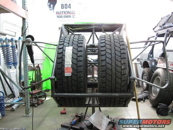 Spare tire carrier holding two large tires, with a partial vehicle visible in the background