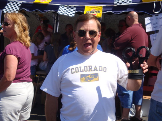 guy in white t-shirt with 'COLORADO' on it holding a trophy made from a piston