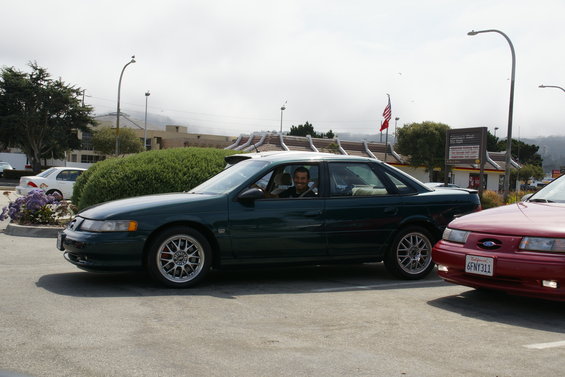 Dark green sedan with aftermarket wheels parked next to a red car