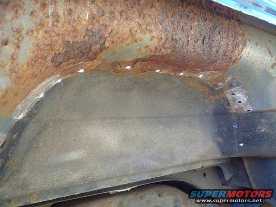 Rusted wheel well interior with visible metal damage and white sealant