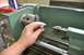 1996 Ford Bronco - A person holds a small metal part near the chuck of a metal lathe.