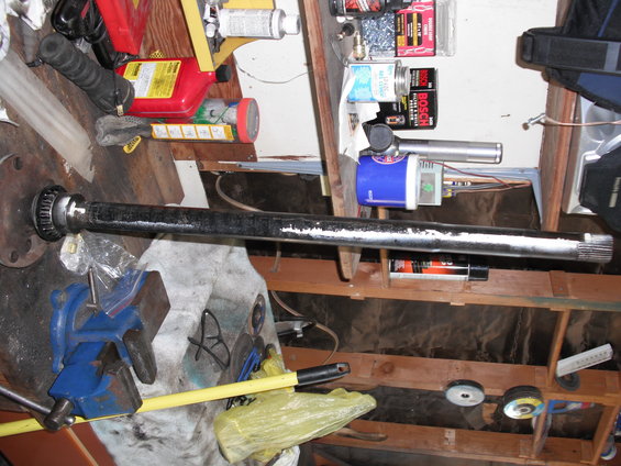 Axle shaft held in a blue vise, with various tools and supplies in the background