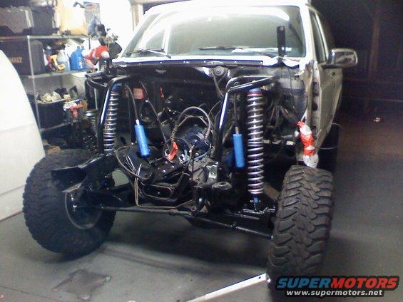 Front end of a vehicle being worked on, with engine removed and suspension exposed