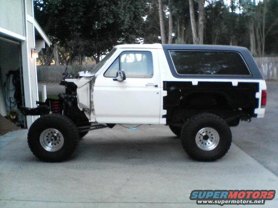Side view of white Ford Bronco missing front end, with black top